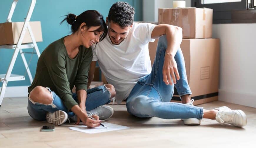 young couple drawing at the blueprints of their new home while talking of the future sitting on the floor.