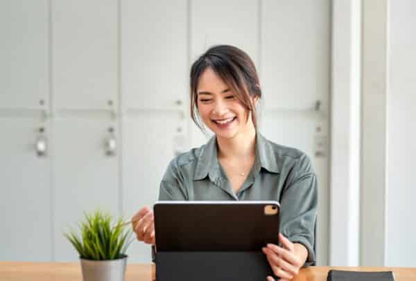 Happy young woman holding a pen using a tablet at the office.